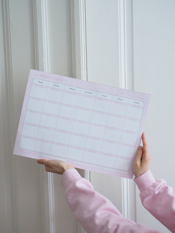 Hände halten den Monatsplaner A3 Schleifchen in Rosa als Schreibtischunterlage
